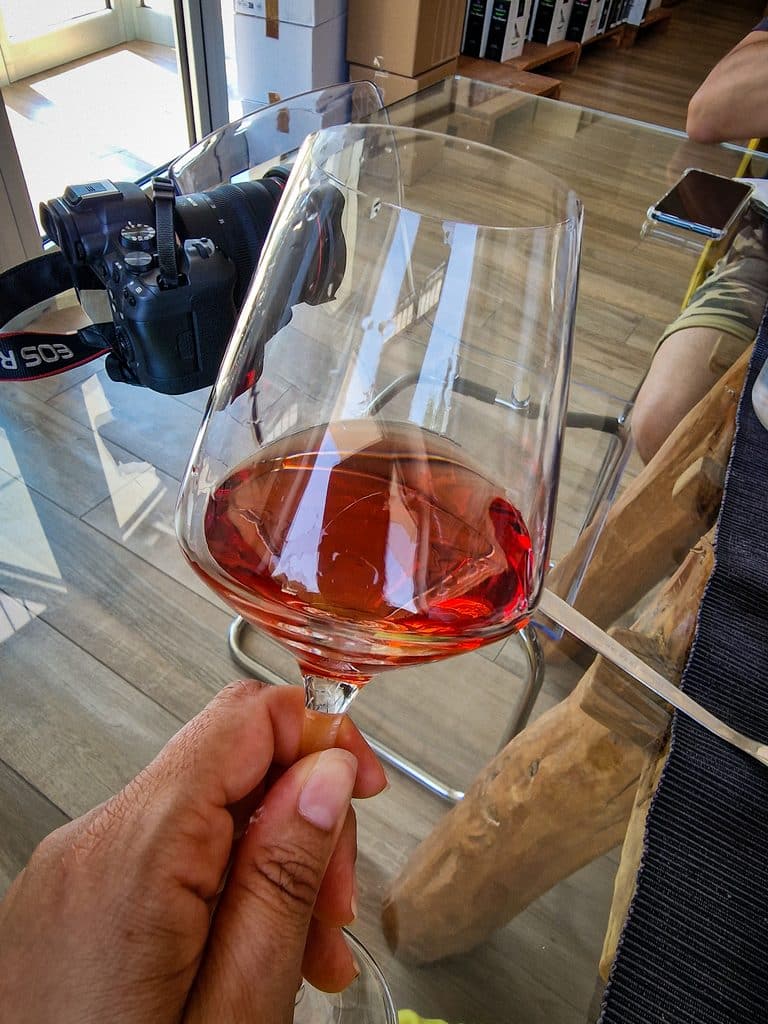 Visita cantina Margiotta - Primo piano di una mano che tiene un calice di cerasuolo su un tavolo in vetro.